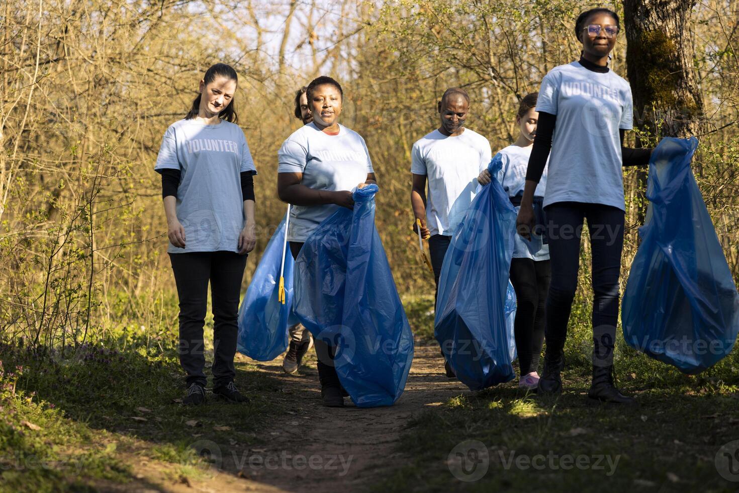 Team of volunteers doing community service to collect garbage and help preserve natural ecosystem, gathering to clean the forest. Diverse group fighting pollution and illegal dumping. photo