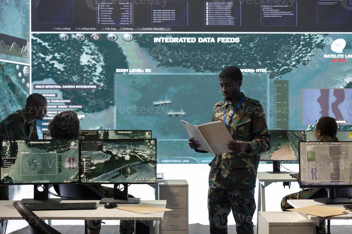 Special operations engineer reading new mission case file brief in control room, working with real time surveillance projection on a big screen. Trooper in army division defense program. photo