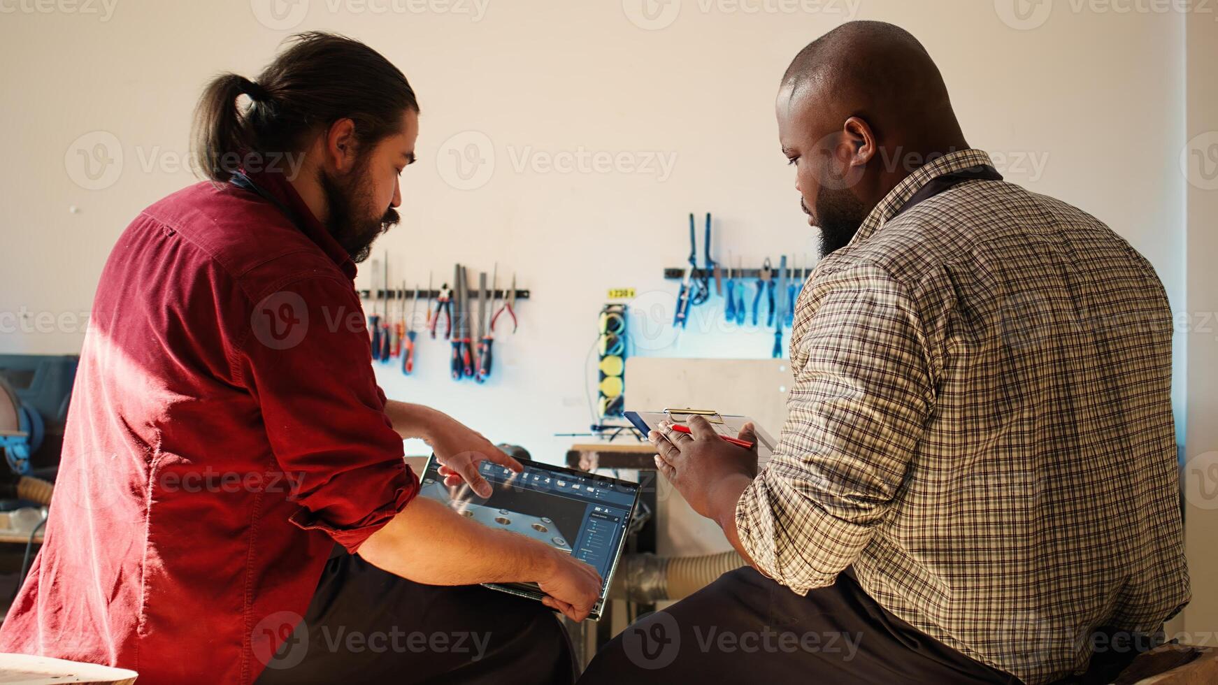 African american artist and colleague comparing wood art schematic with CAD software 3D render on laptop. Carpenters at work crosscheck drawing on clipboard with notebook blueprint, camera B photo