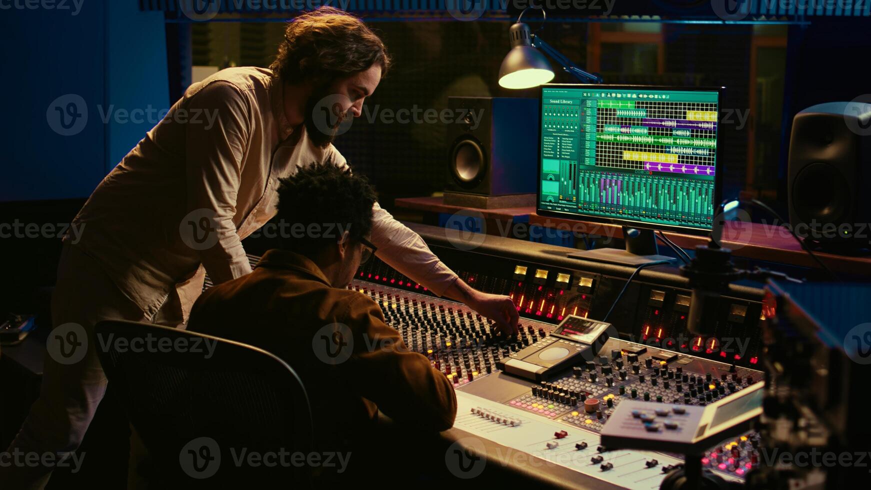 Diverse team of musician and audio technician creating a hit song, working in professional music studio. Artist with producer editing and recording tracks on mixing console panel. Camera B. photo