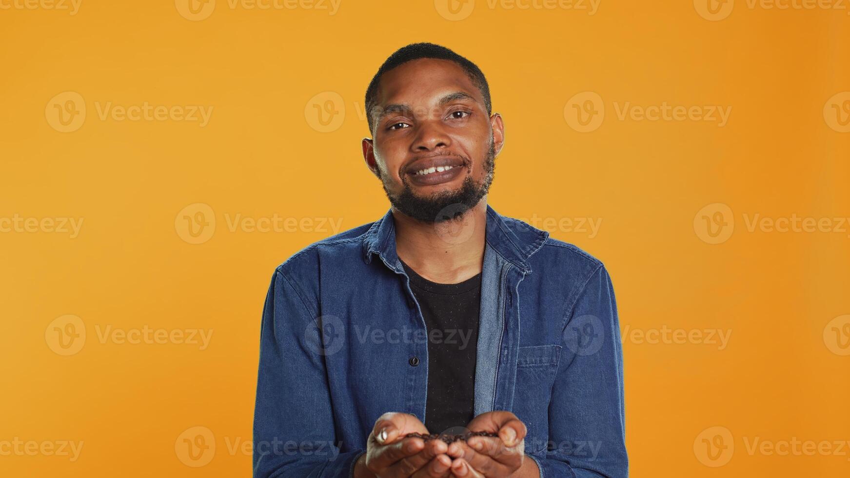 Coffee enthusiast looks at aromatic roasted beans against orange background, promoting cold brew at a coffee shop or cafeteria. Enjoying eco friendly delicious black seeds. Camera A. photo