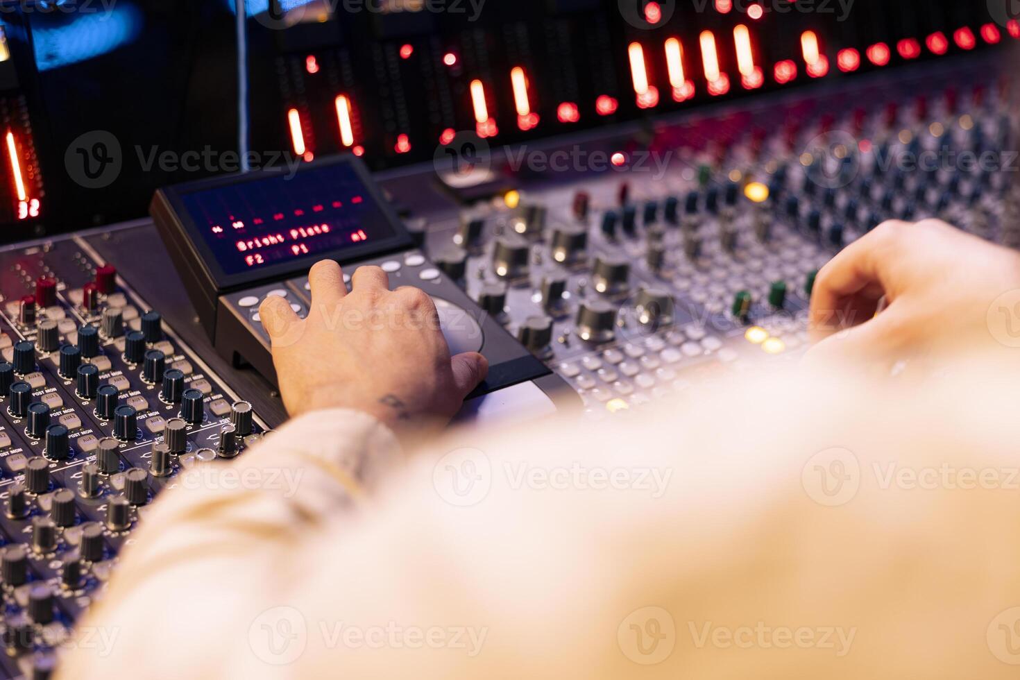Tracking engineer pressing faders and buttons on control desk to balance sounds and add effects in post production, creating new music. Technical expert working with sliders in professional studio. photo