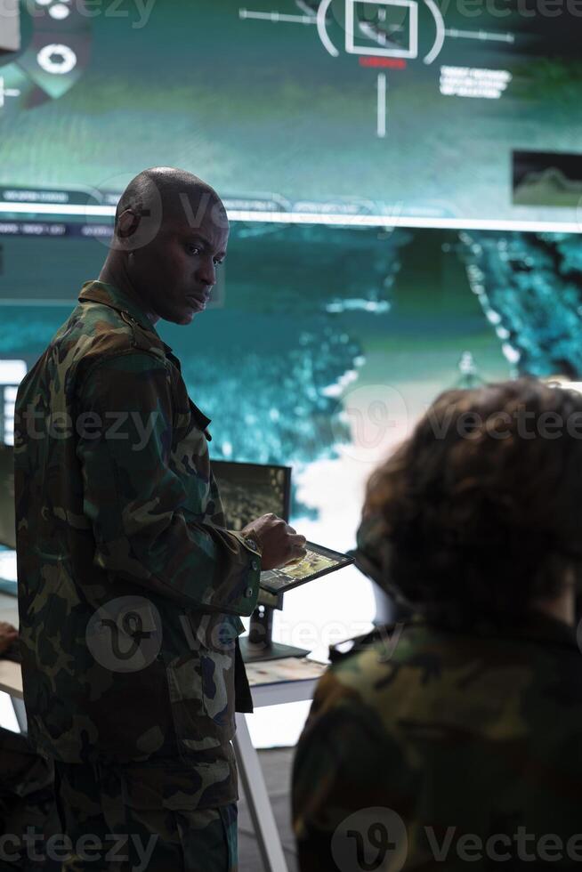 Infantry unit trooper studying the reconnaissance activity in control center, soldiers work with a big screen to analyze real time data from CCTV radar systems. Supply and transportation logistics. photo