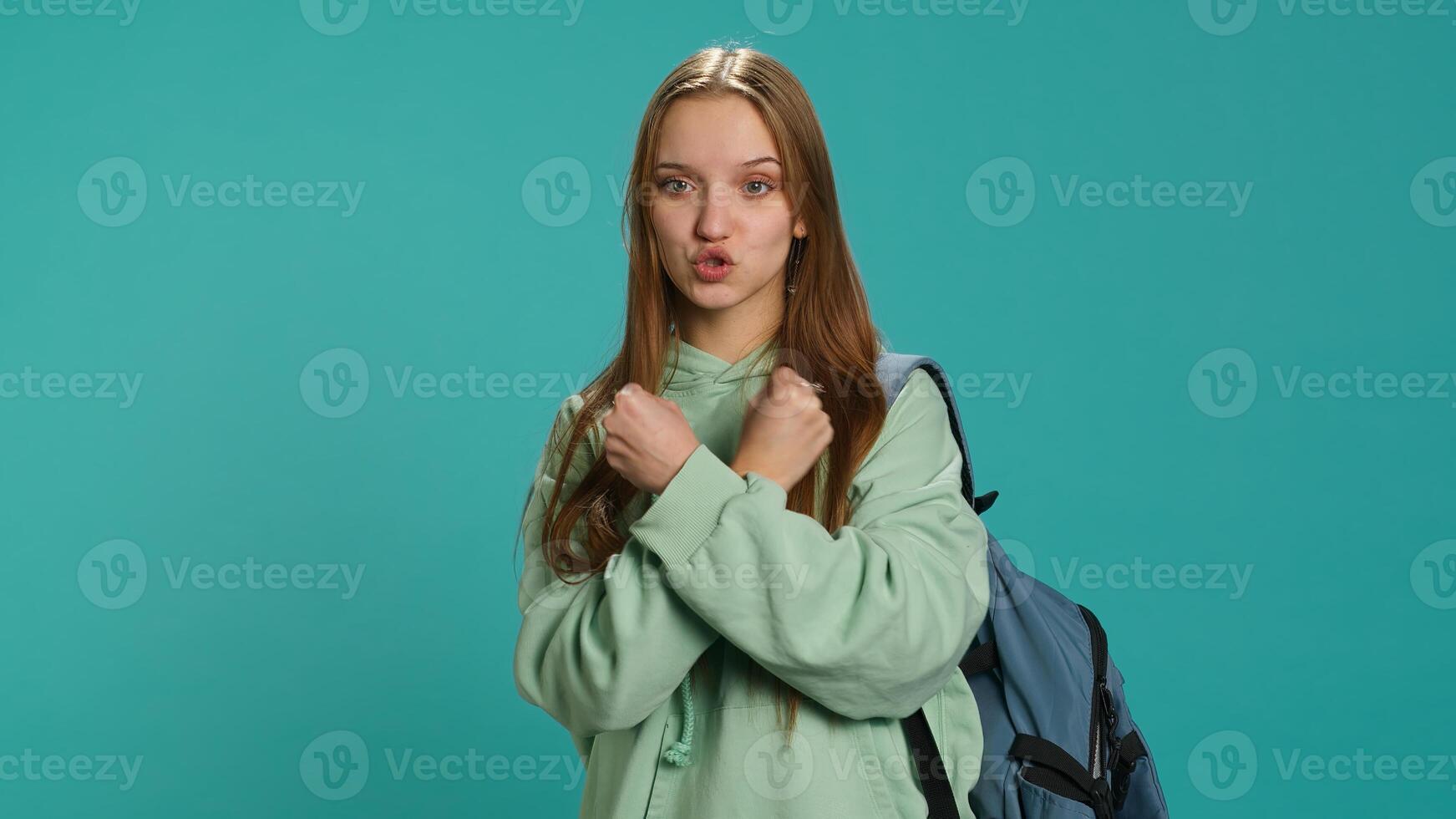 Assertive woman shows letter X with arms crossed, staying in warrior stance, showing fierceness. Firm young person using negative body language to signal rejection, studio background, camera A photo