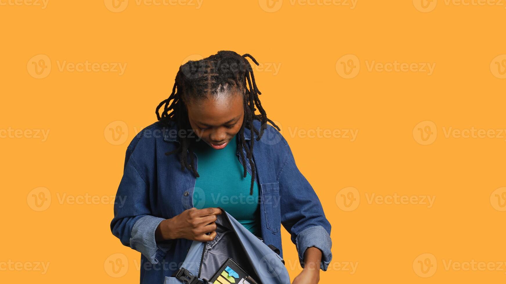 Portrait of happy woman searching through backpack, looking for school materials, studio background. Jolly girl taking out university supplies out of rucksack, preparing for college, camera A photo