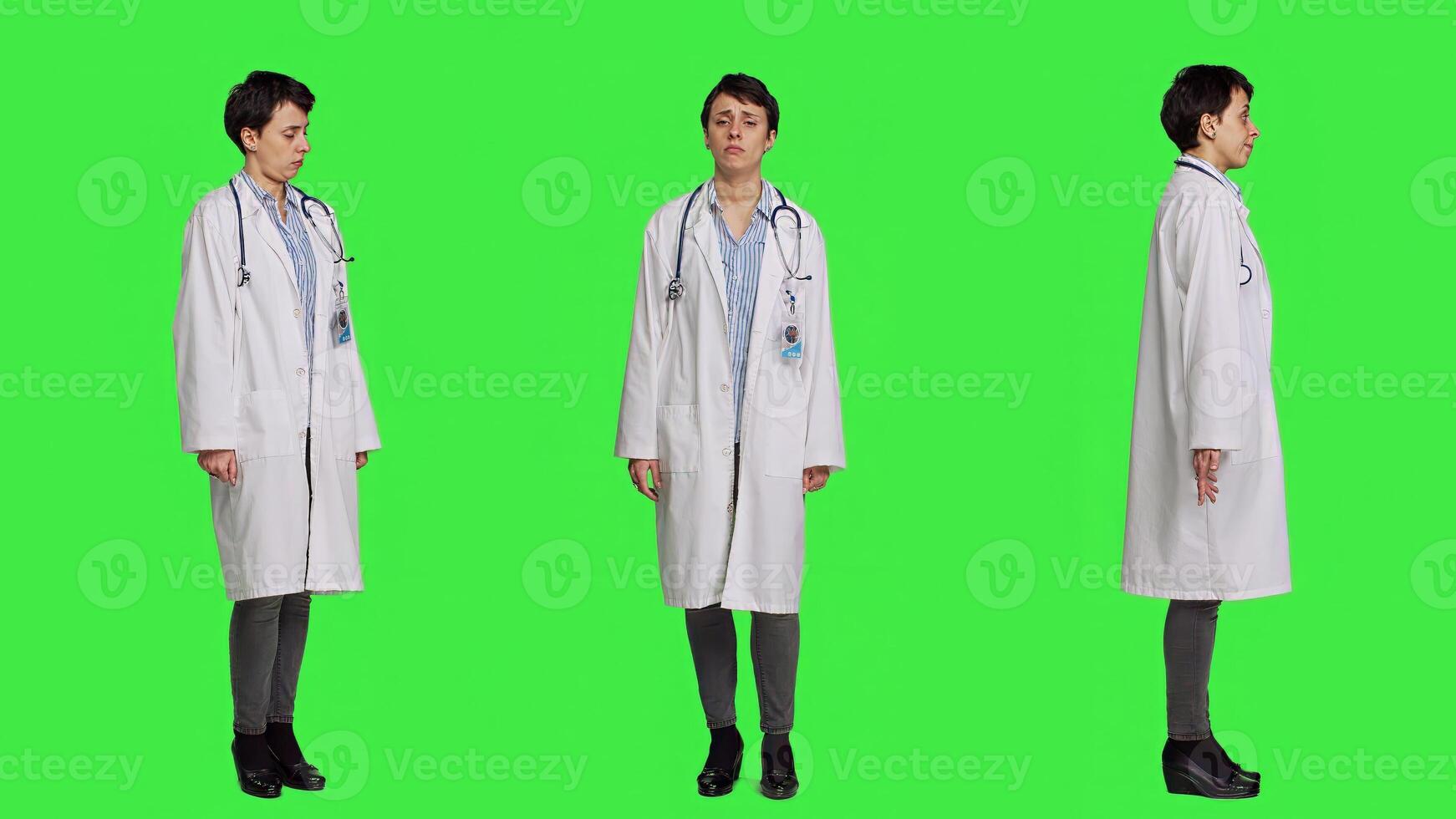 Physician saying no and showing negative reaction symbol in studio, wearing a white coat and standing against greenscreen backdrop. Woman medic feeling displeased, rejection sign. Camera A. photo