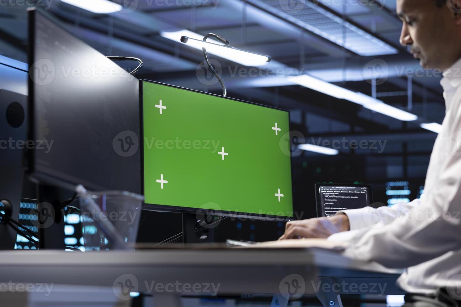 Indian man in data center using green screen computer to check for server performance issues. IT expert in server hub fixing errors slowing down hardware using chroma key PC photo