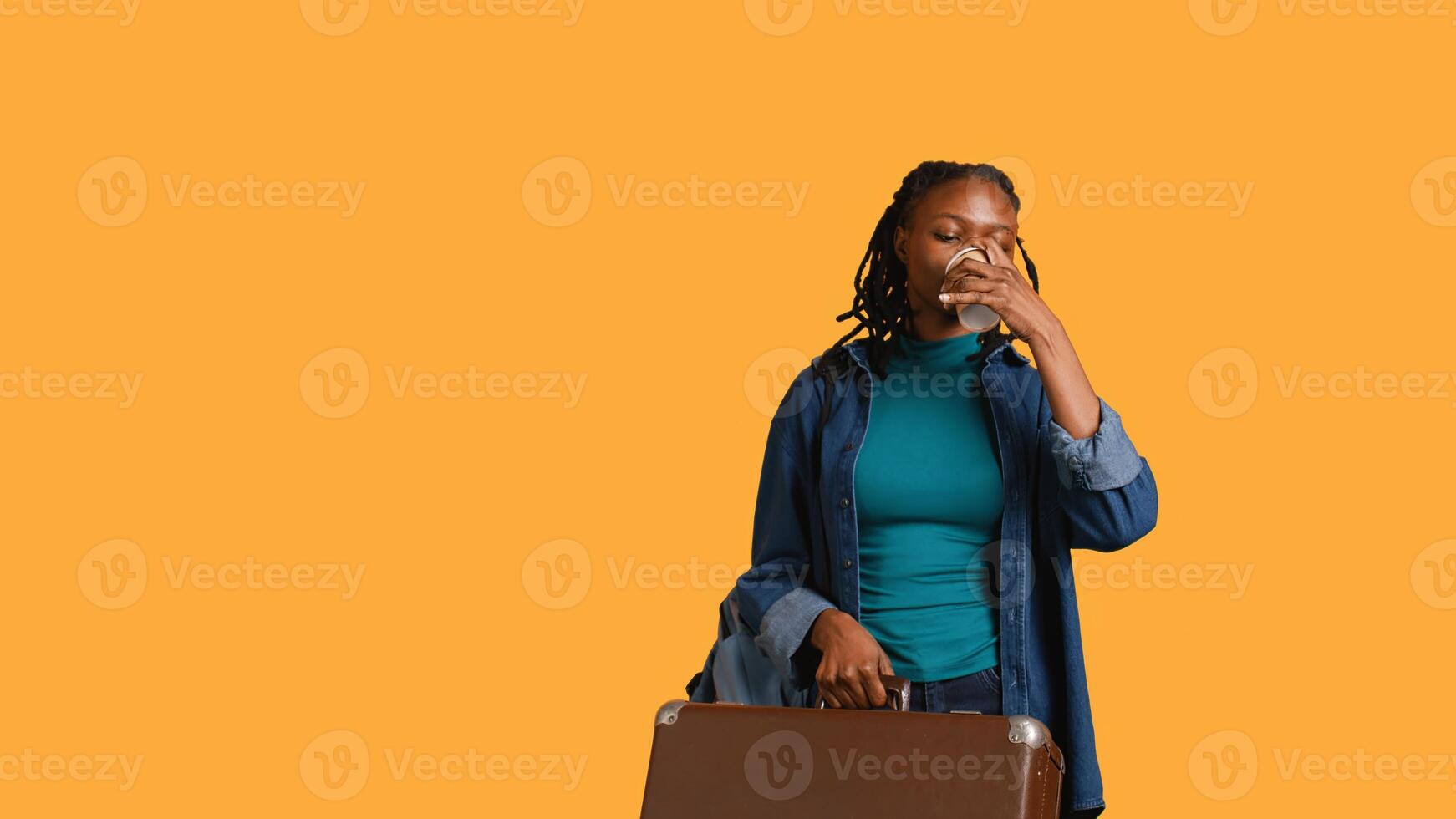 Tired girl travelling with suitcase, drinking coffee to wake up. Sleepy woman using caffeinated beverage to gain energy, going abroad with briefcase, studio background, camera B photo