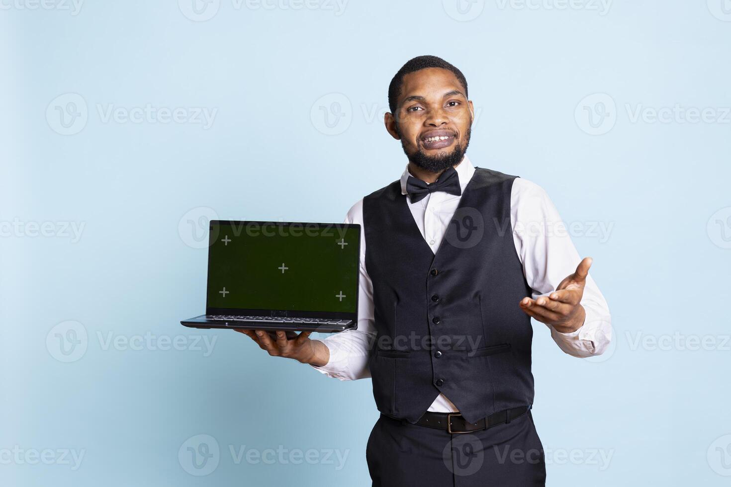 Doorkeeper bellboy holding a laptop with green screen in studio, presenting isolated chroma key display while he works in hospitality industry at a five star hotel. Professional staff. photo