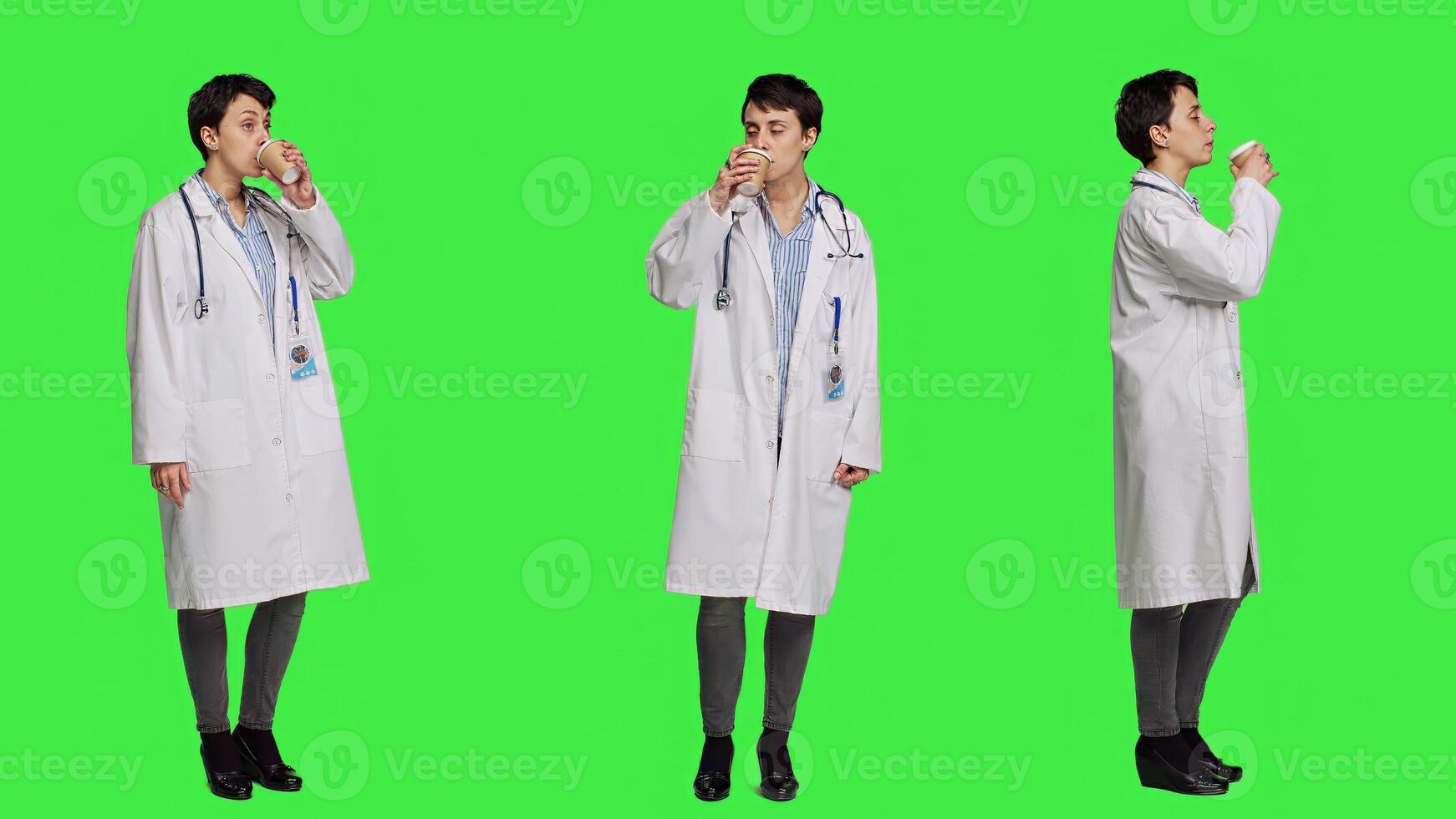 Happy medic serving hot coffee cup as refreshment against greenscreen backdrop, wearing white coat and drinking caffeine beverage. General practitioner enjoying drink, medical expertise. Camera A. photo