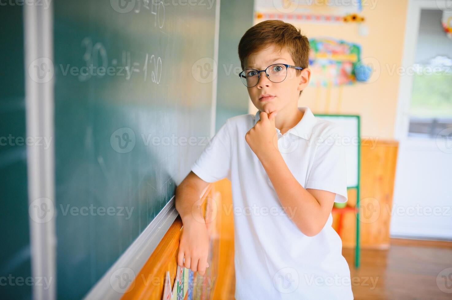 Cute little schoolboy diligent write chalk solve math problem dressed stylish uniform classroom blackboard background photo