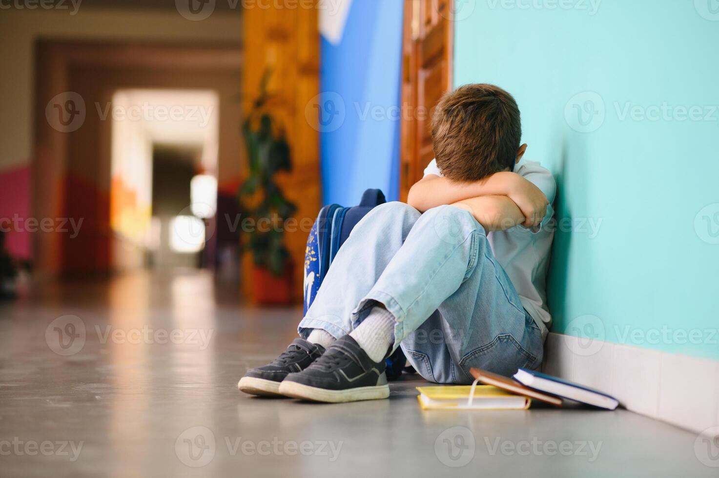 Young boy sitting alone with sad feeling at school. Bullying, discrimination and racism concept with copy space photo