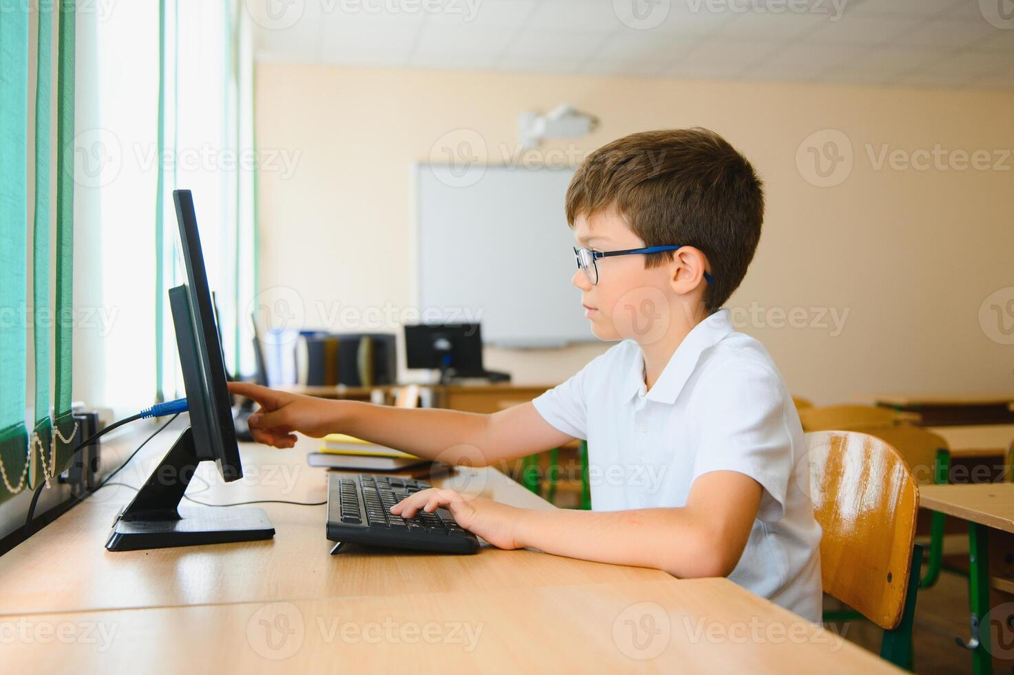 Teenage boy smiling while using computer at desk in classroom photo