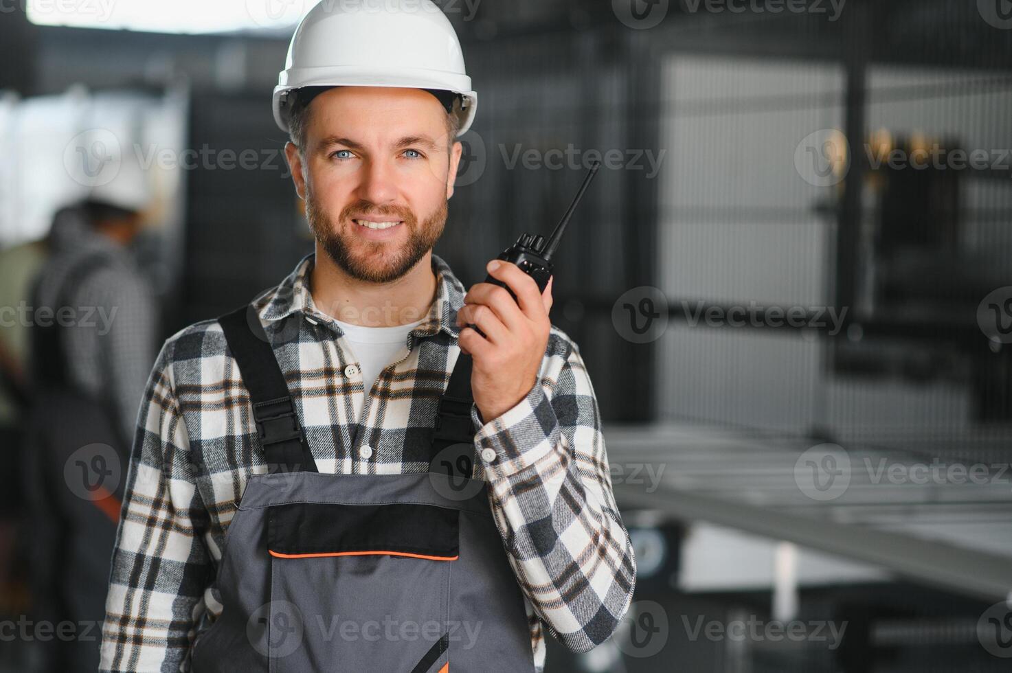 Smiling and happy employee. Portrait of industrial worker indoors in factory. Young technician with white hard hat photo