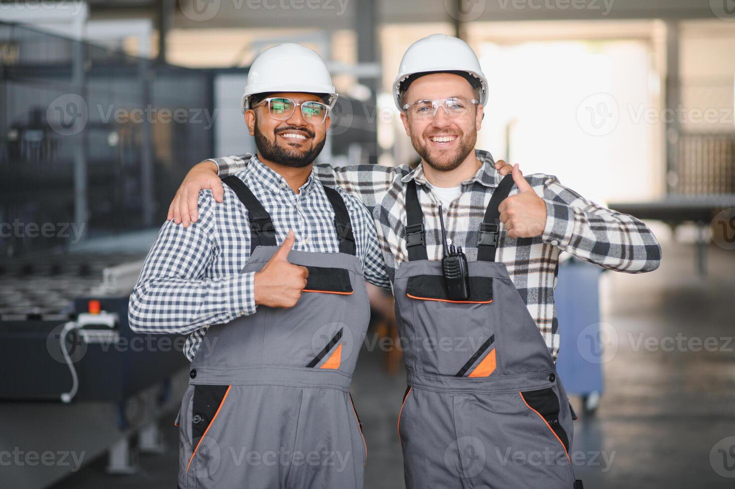 Two happy international workers in overalls hug each other against a factory background photo