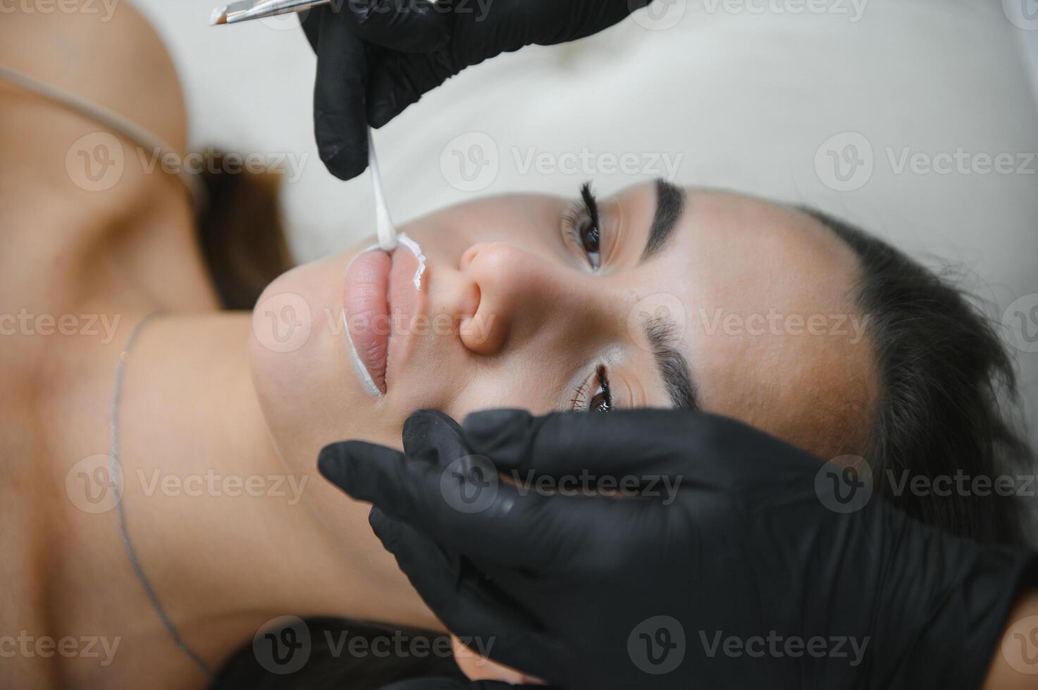 The permanent makeup artist draws a white outline on the lips before the procedure begins photo