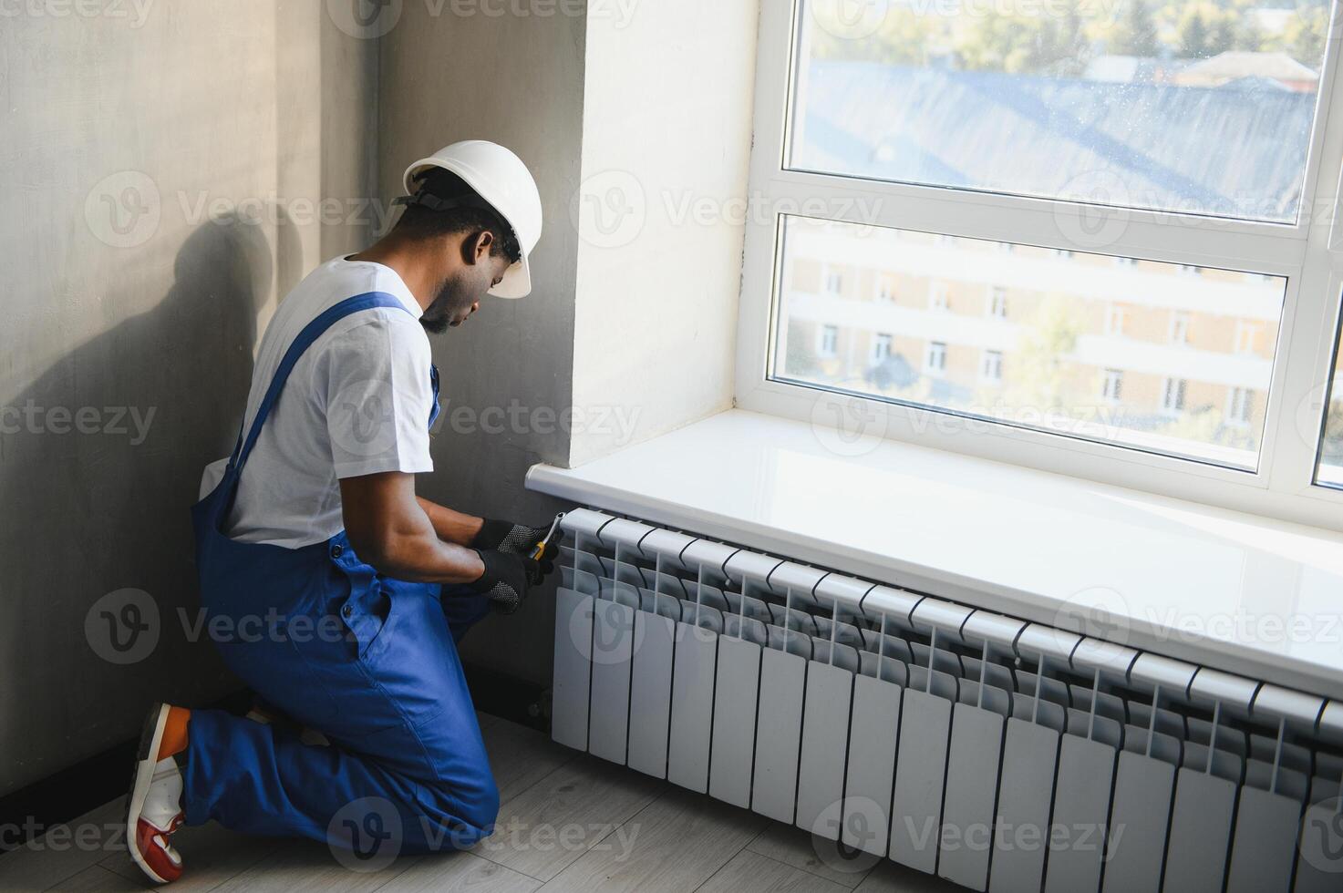 Repair heating radiator close-up. African man repairing radiator with wrench. Removing air from the radiator photo