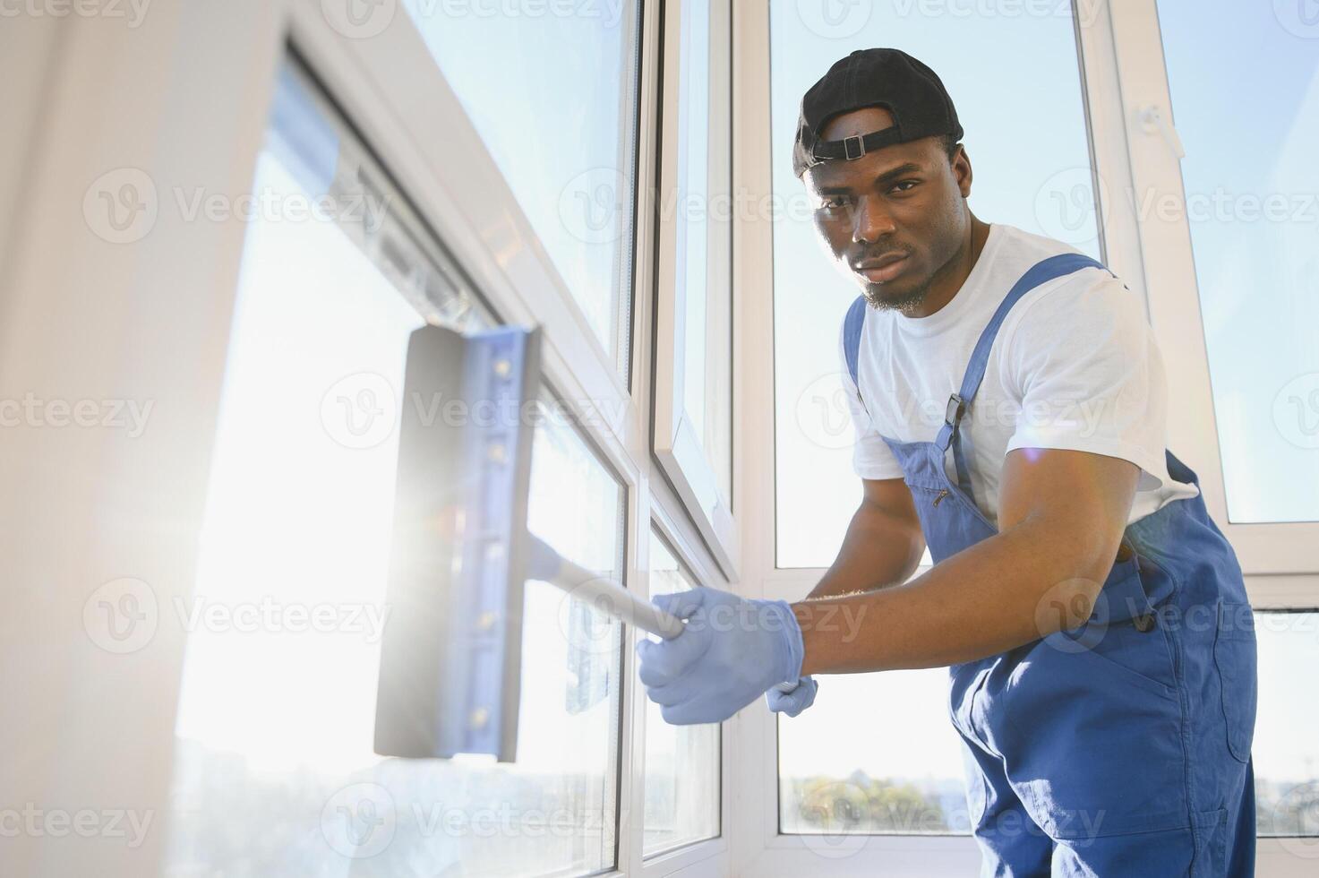 African Male professional cleaning service worker in overalls cleans the windows with special equipment photo