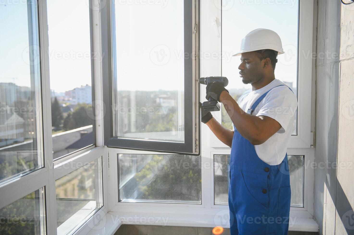 Workman in overalls installing or adjusting plastic windows in the living room at home photo