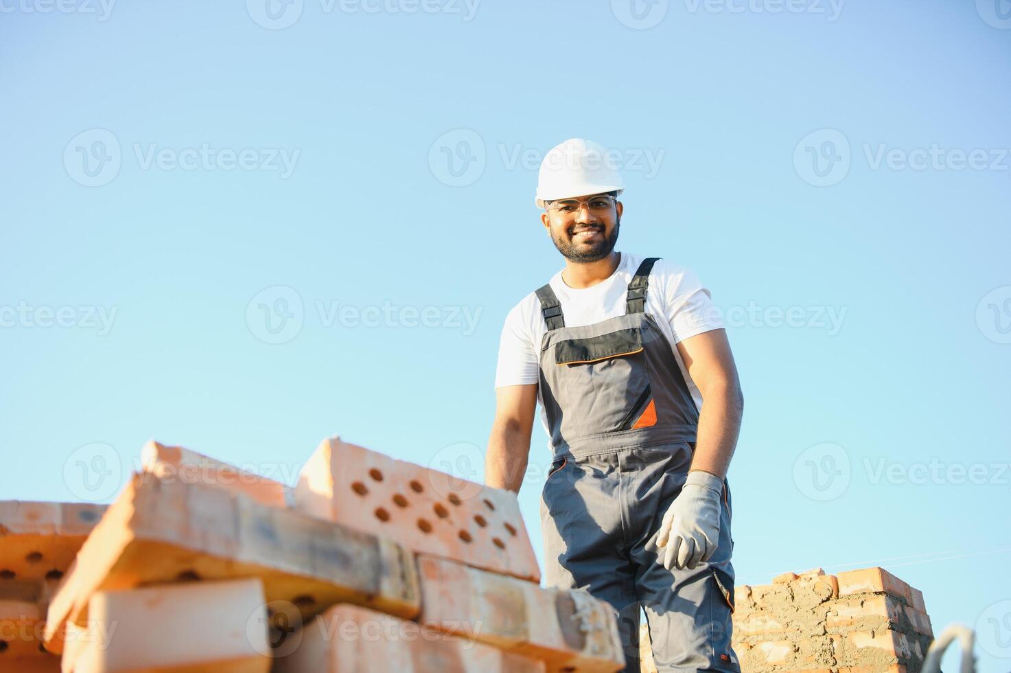 Indian Construction worker man in work clothes and a construction helmet. Portrait of positive male builder in hardhat working at construction site photo