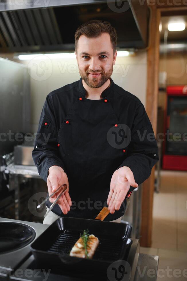 Chef in hotel or restaurant kitchen cooking, he is cutting meat or steak photo