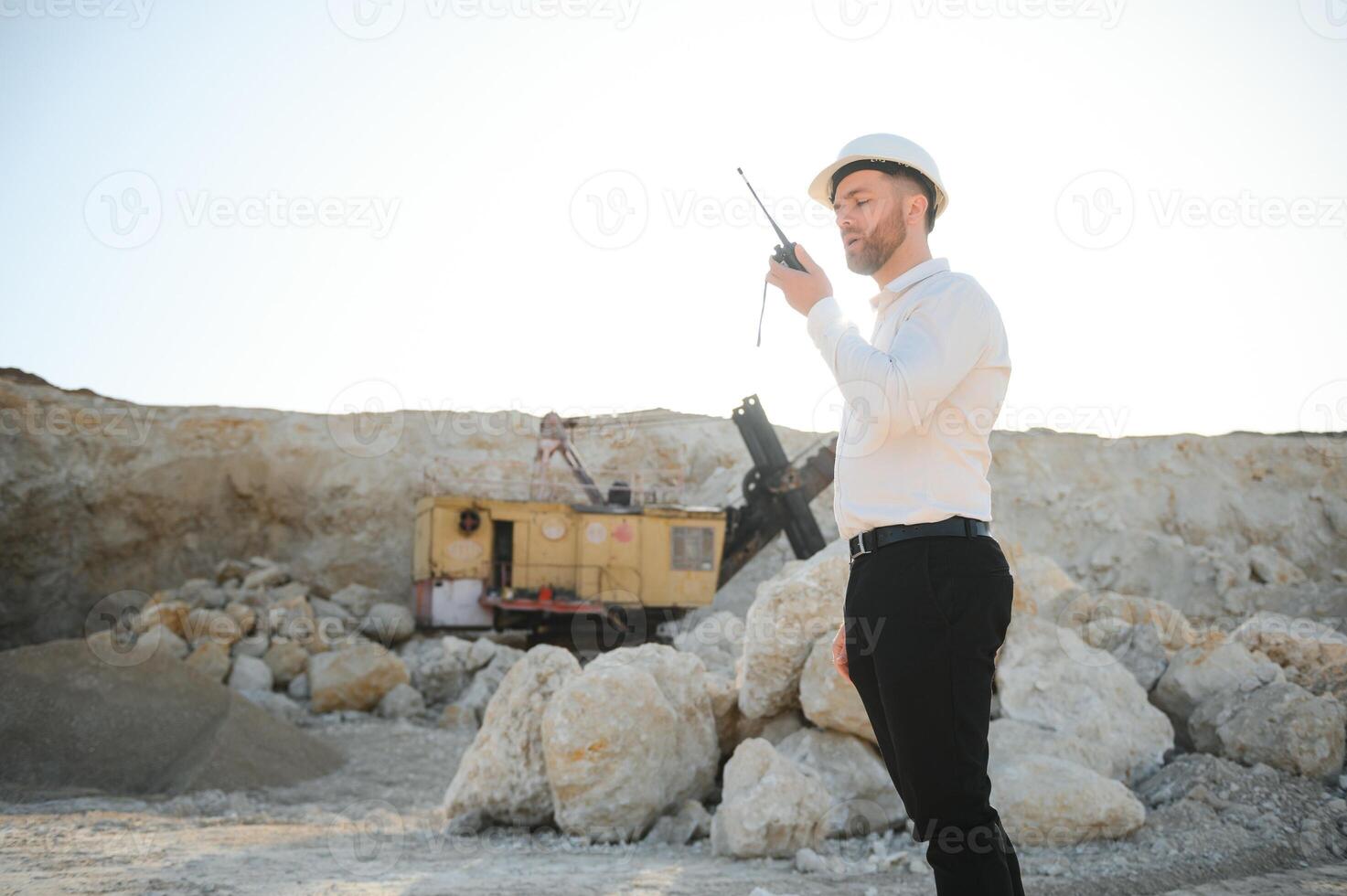 A worker in a helmet stands on the background of an excavator in a quarry photo