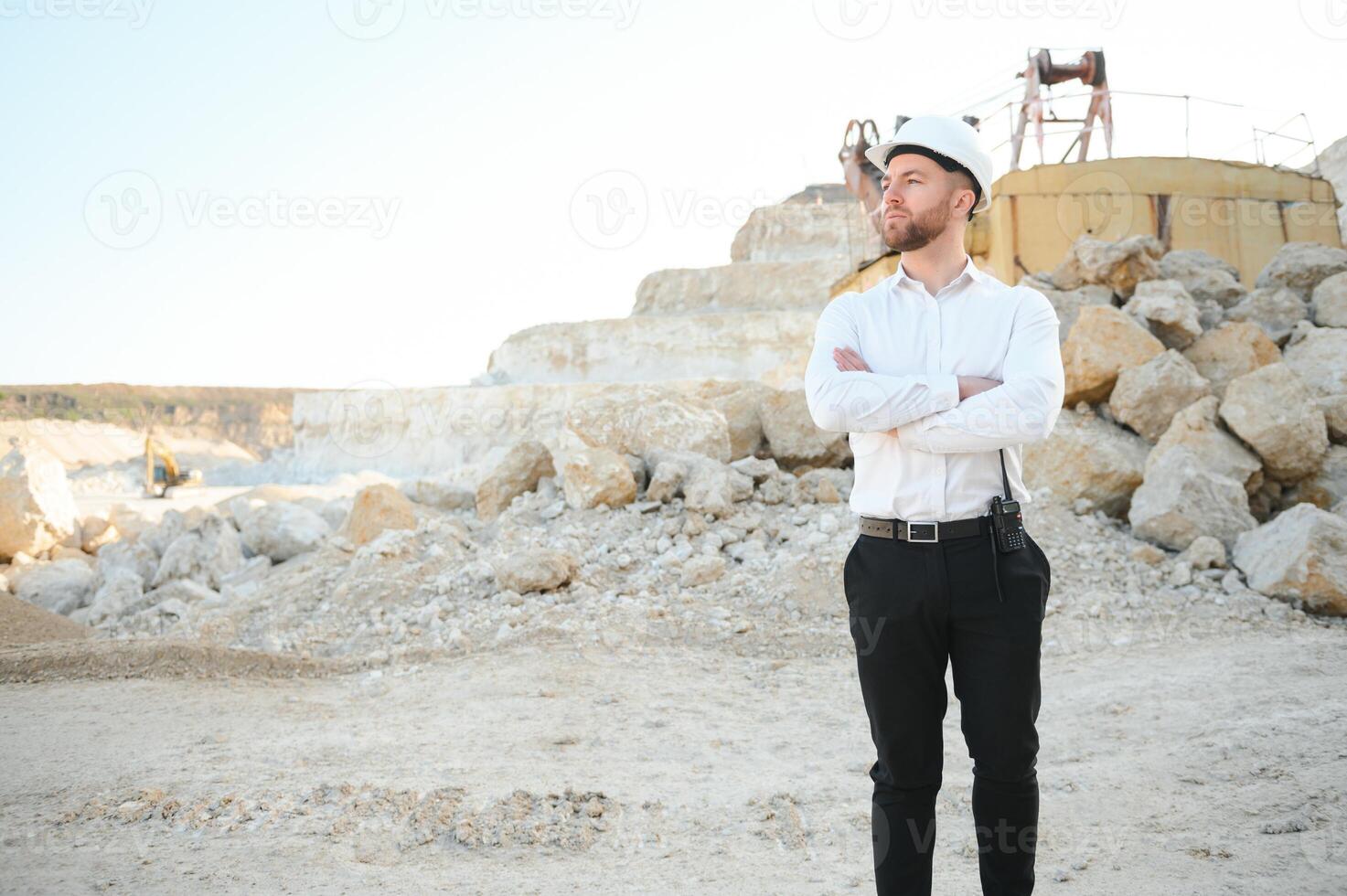 A worker in a helmet stands on the background of an excavator in a quarry photo