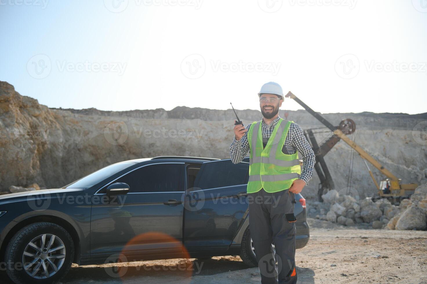 A worker in a helmet stands on the background of an excavator in a quarry photo
