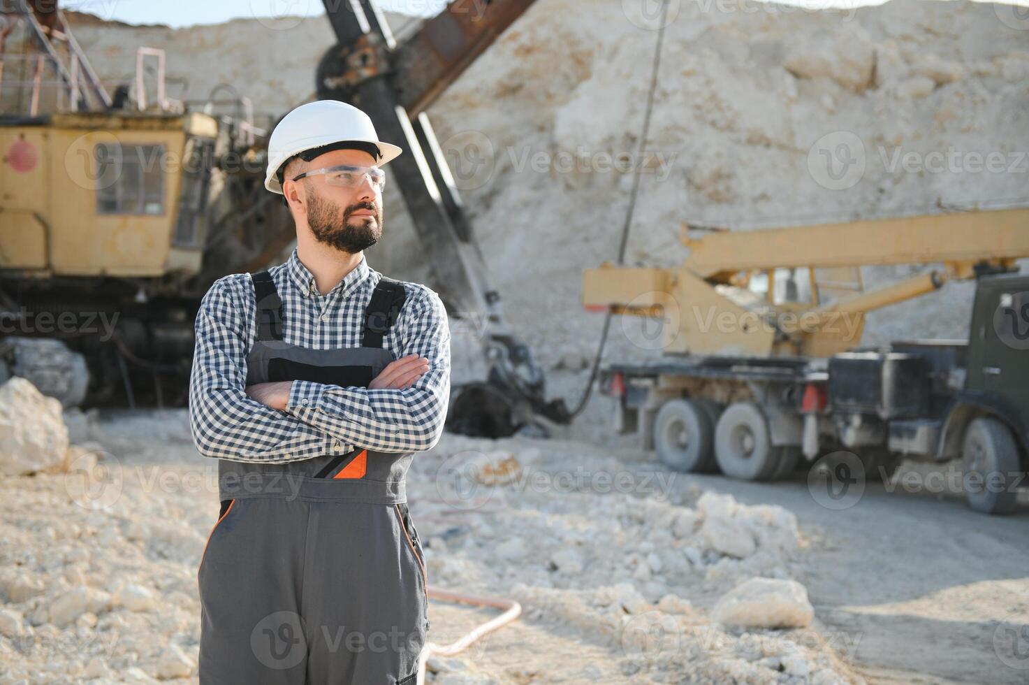 A worker in a helmet stands on the background of an excavator in a quarry photo