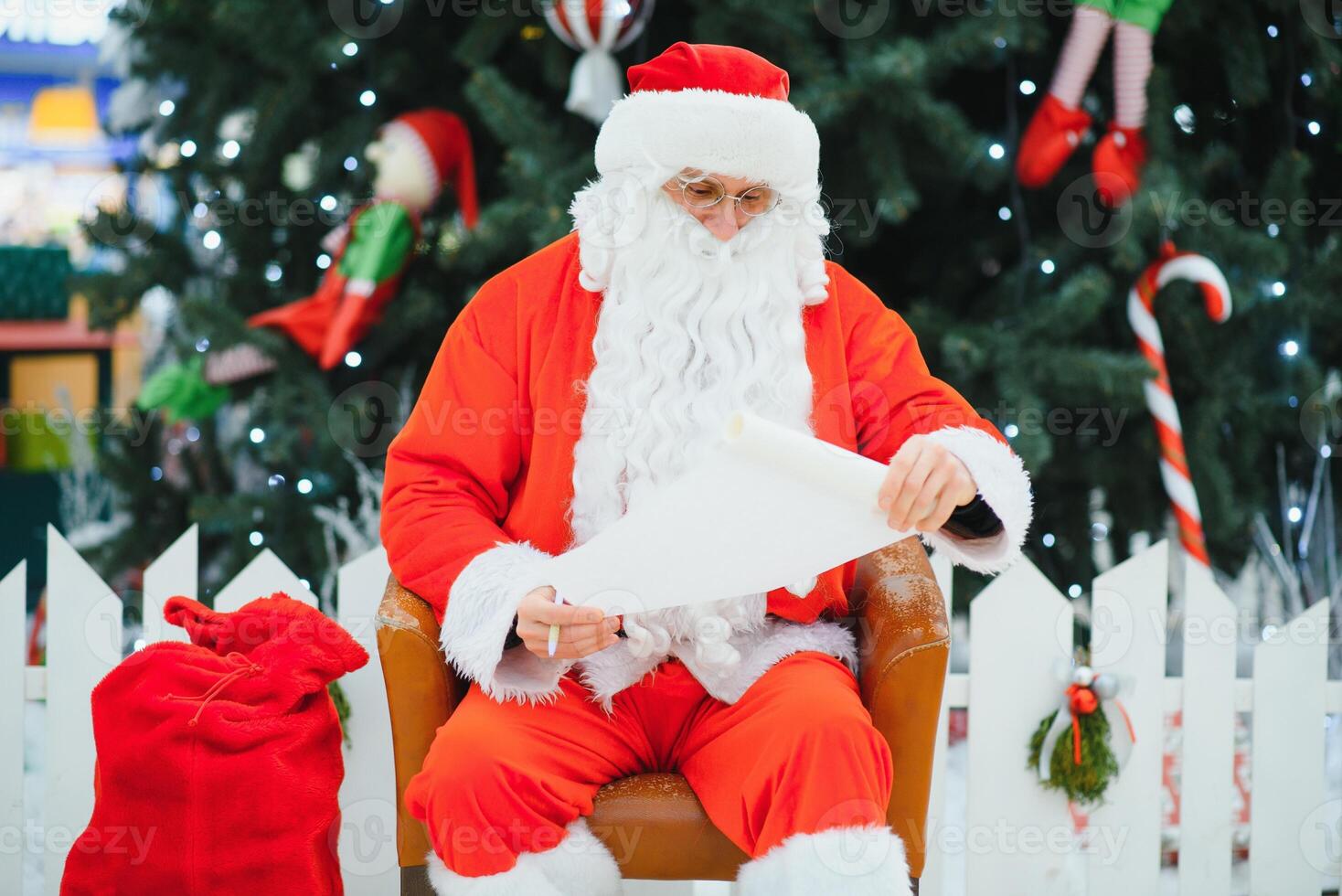 Santa Claus sitting on the background of the Christmas tree in the lobby of the modern shopping mall. Bokeh basic background for design. photo