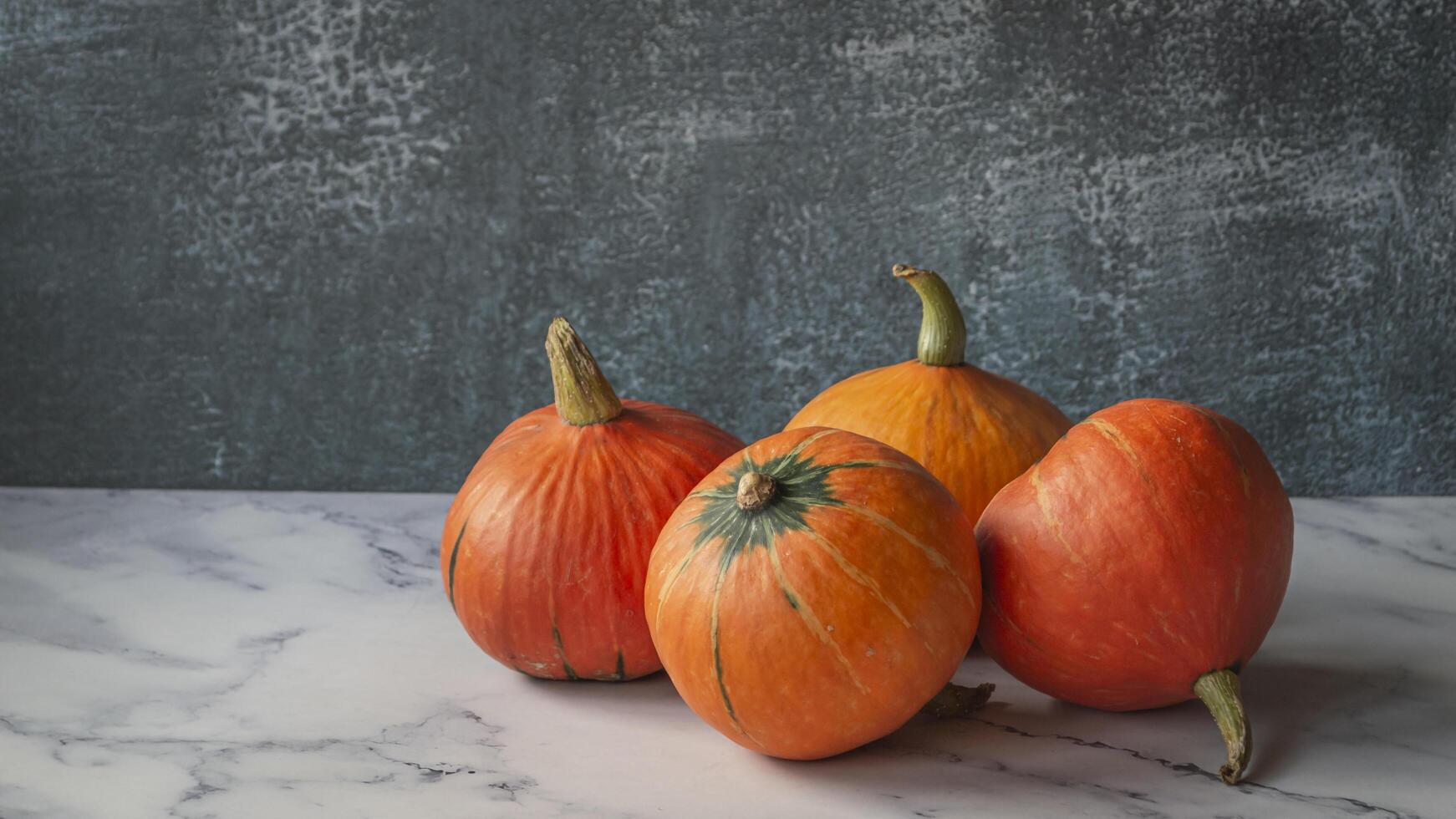 three pumpkins on a table with a gray wall photo