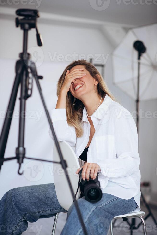 Young woman with a camera, ready to take photos in a professional studio. The lighting setup emphasizes her focus and dedication to her craft.