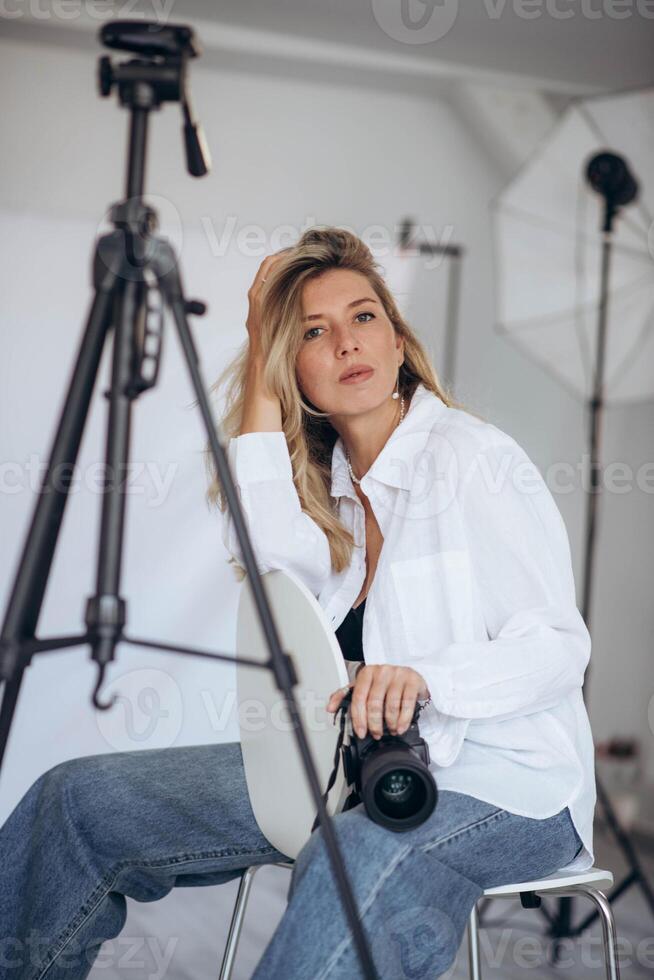 Young woman with a camera, ready to take photos in a professional studio. The lighting setup emphasizes her focus and dedication to her craft.