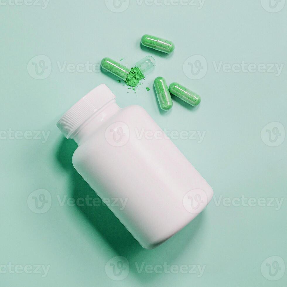 A bottle of green pills and a green capsule on a green background photo