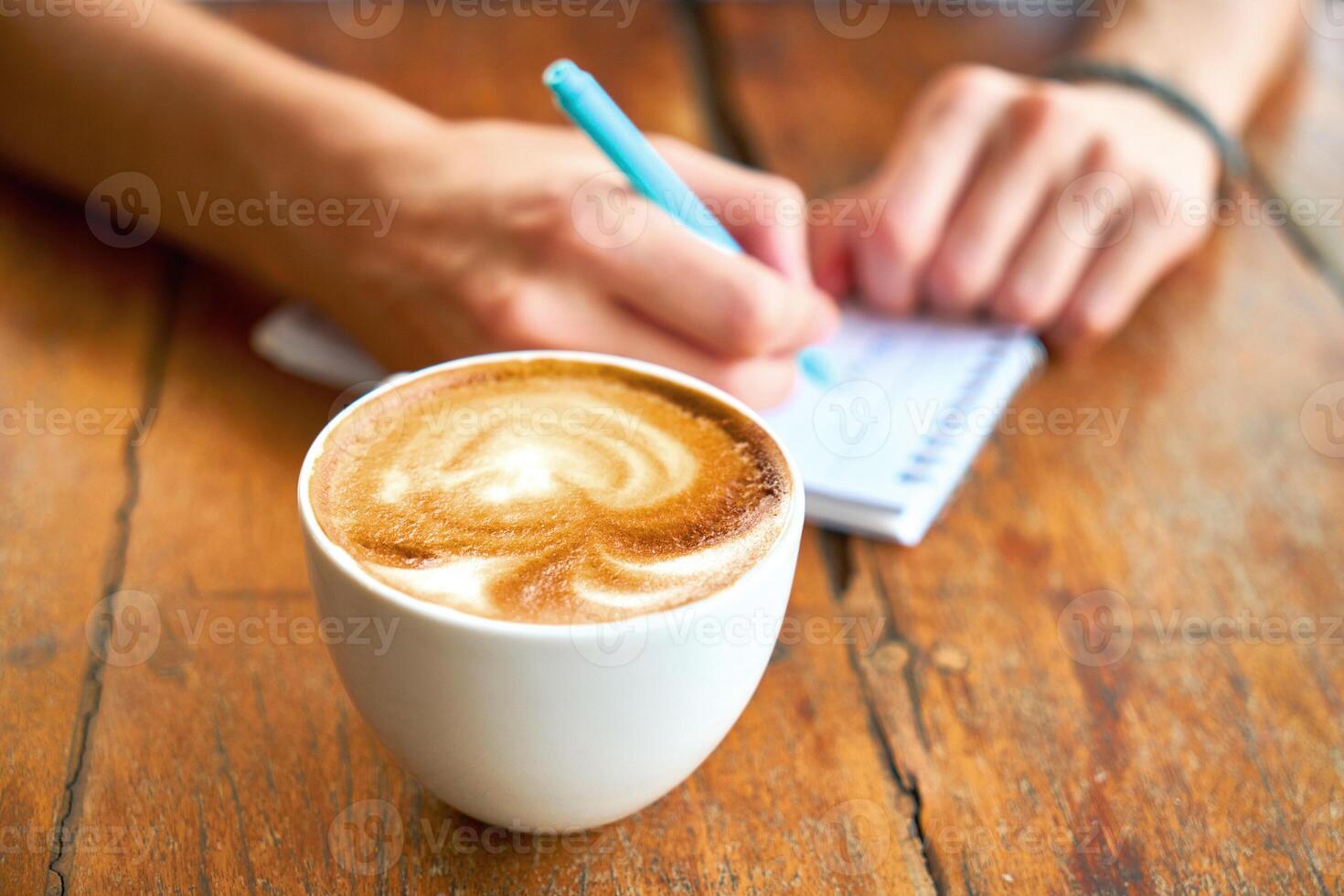 A man writing in a notebook and a cup of coffee on a wooden table photo