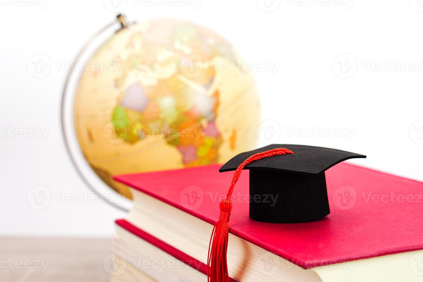 A Graduation cap placed on a stack of books and blurred globe behind. It is the concept of education, knowledge, learning and successful. photo