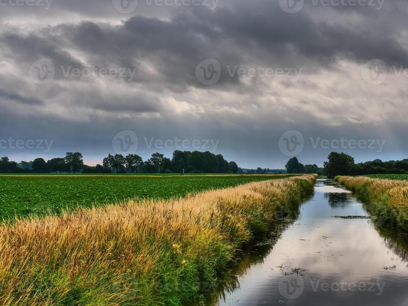A canal in the middle of a field with dark clouds photo