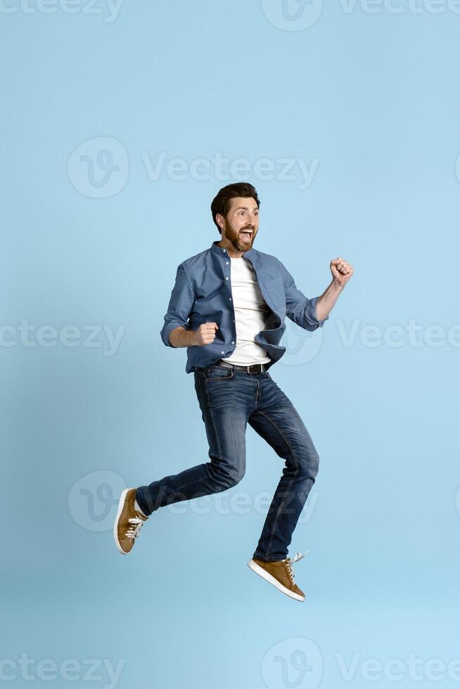 Excited young man jumping and celebrating with fists in the air photo