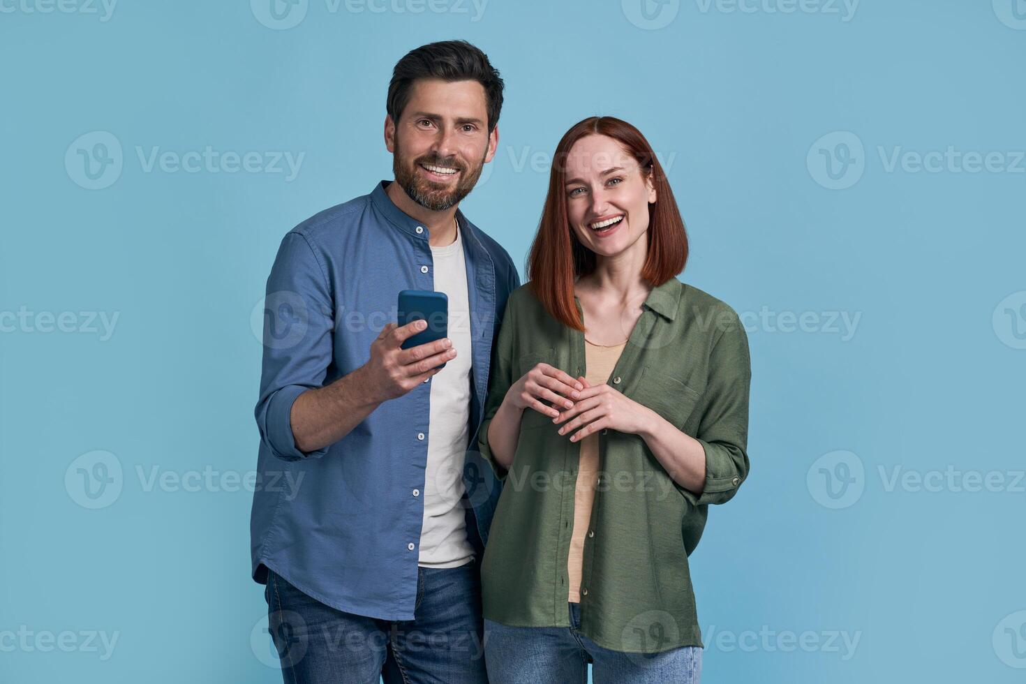 Happy couple smiling and browsing social media on smartphone against blue background photo