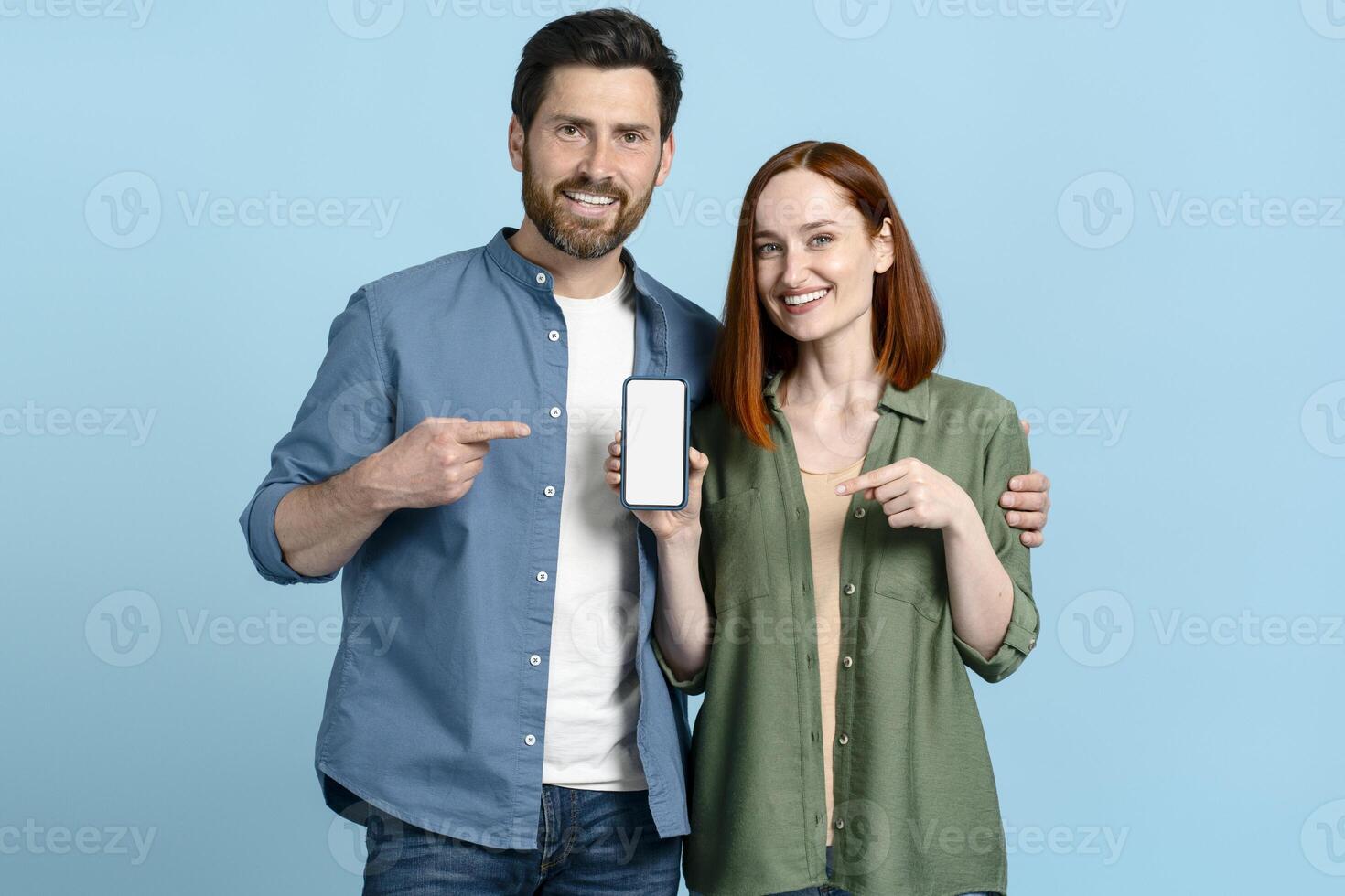 Happy couple pointing at smartphone with empty screen on blue background photo