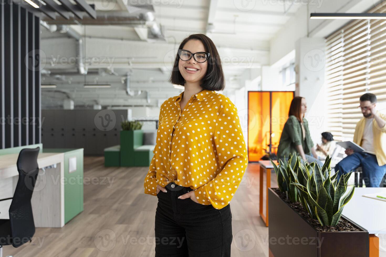 Successful businesswoman smiling in modern open plan office with coworkers in background photo
