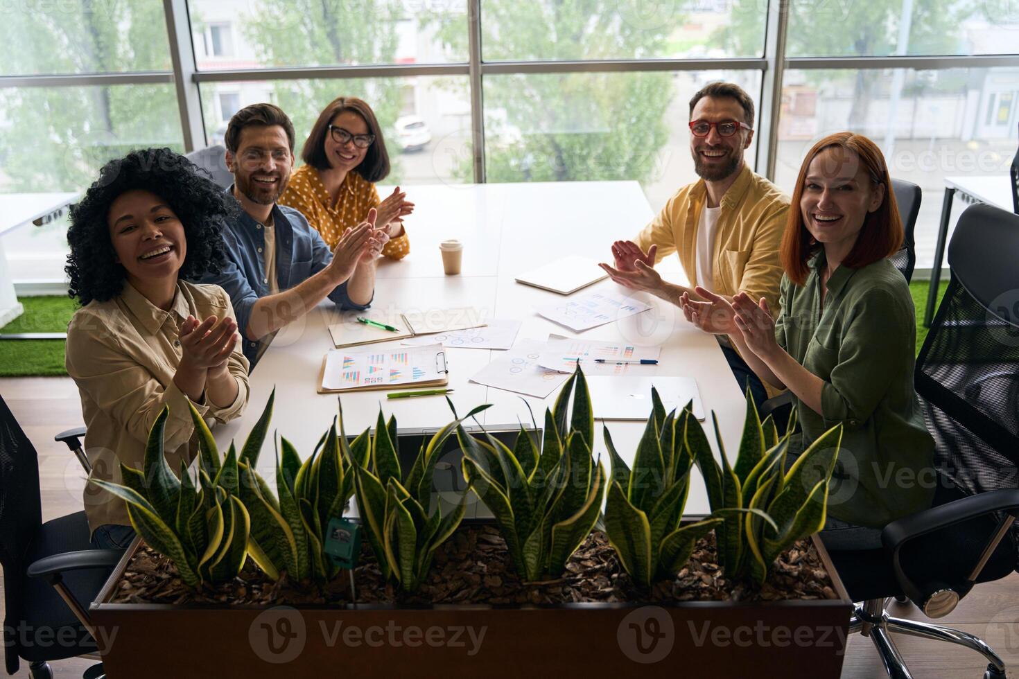 Happy business people clapping hands sitting at office desk photo