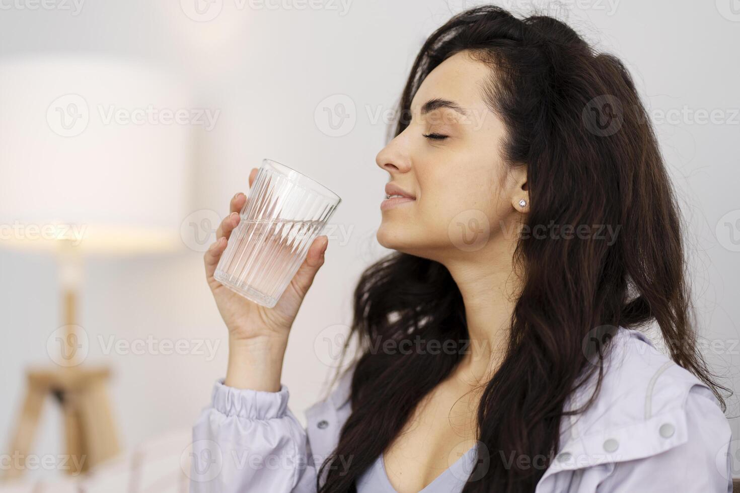 Beautiful young woman enjoying drinking fresh water from glass at home photo