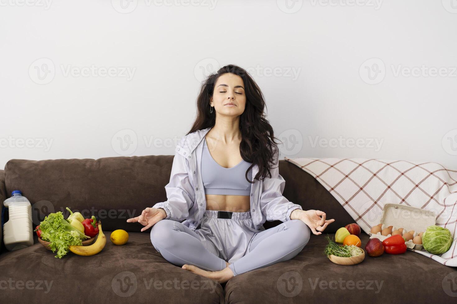 Young woman meditating on sofa surrounded by healthy food photo