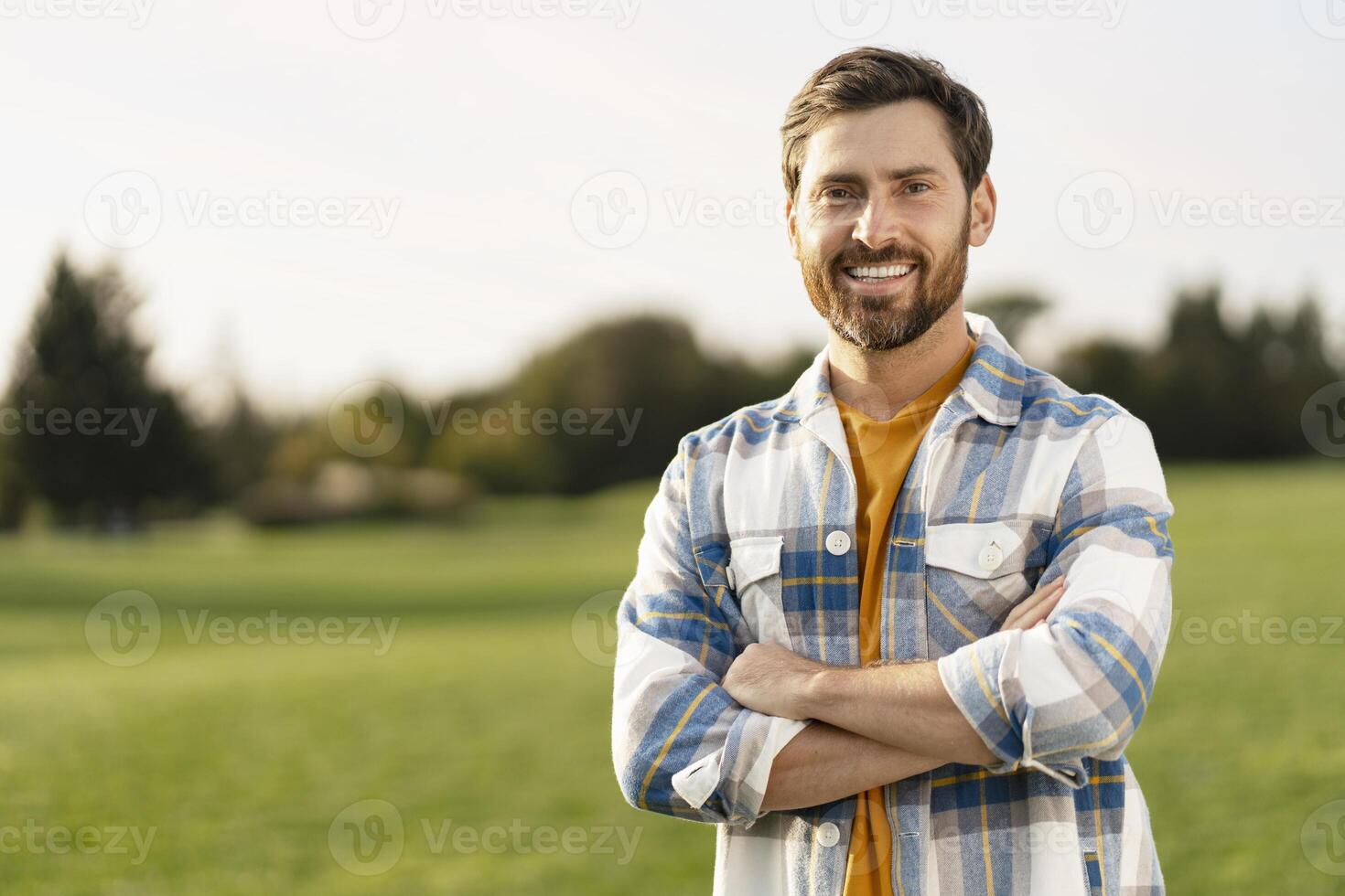 Portrait of a smiling farmer standing in green field with crossed arms photo