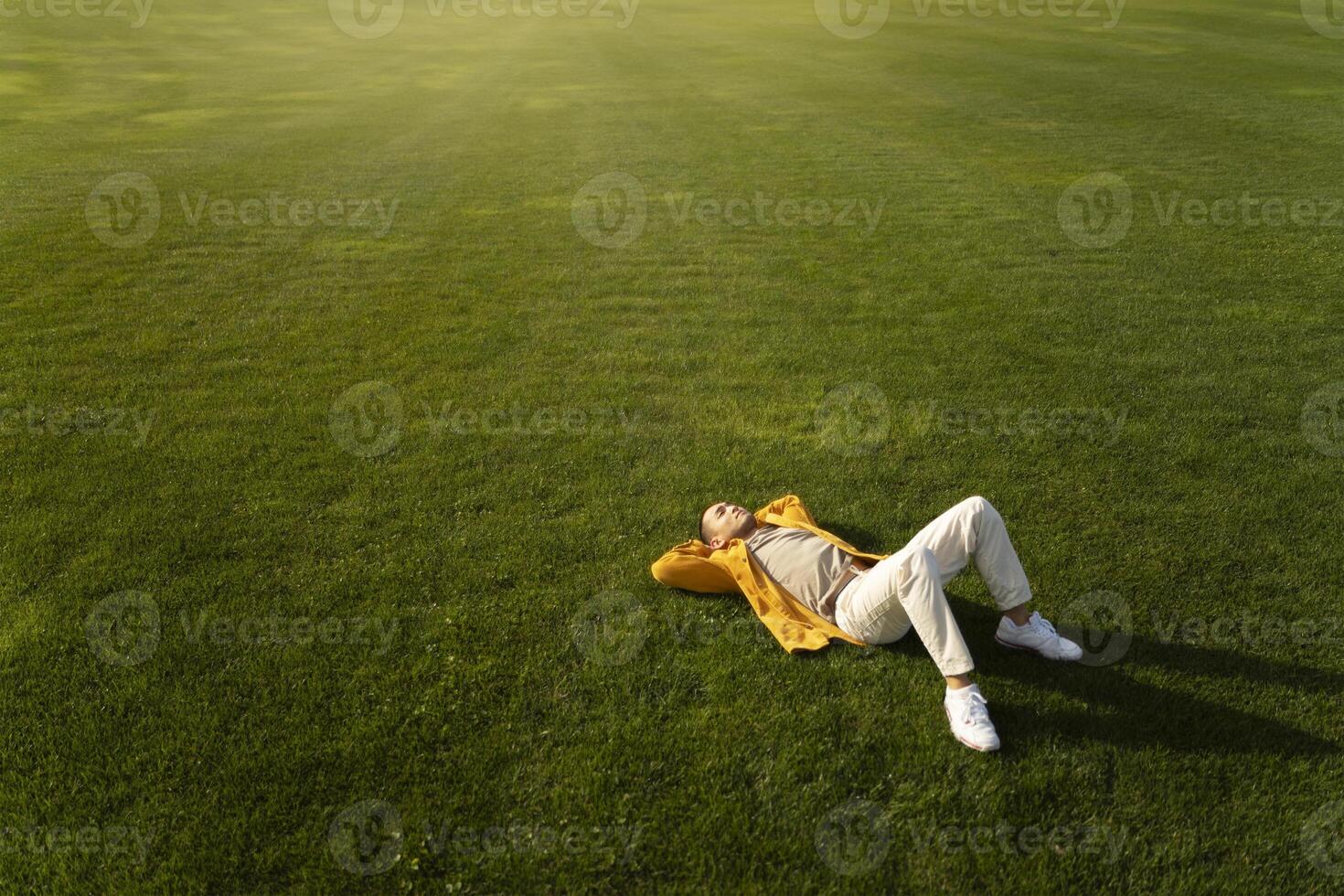 Young man relaxing lying down on green grass field looking up at sky photo