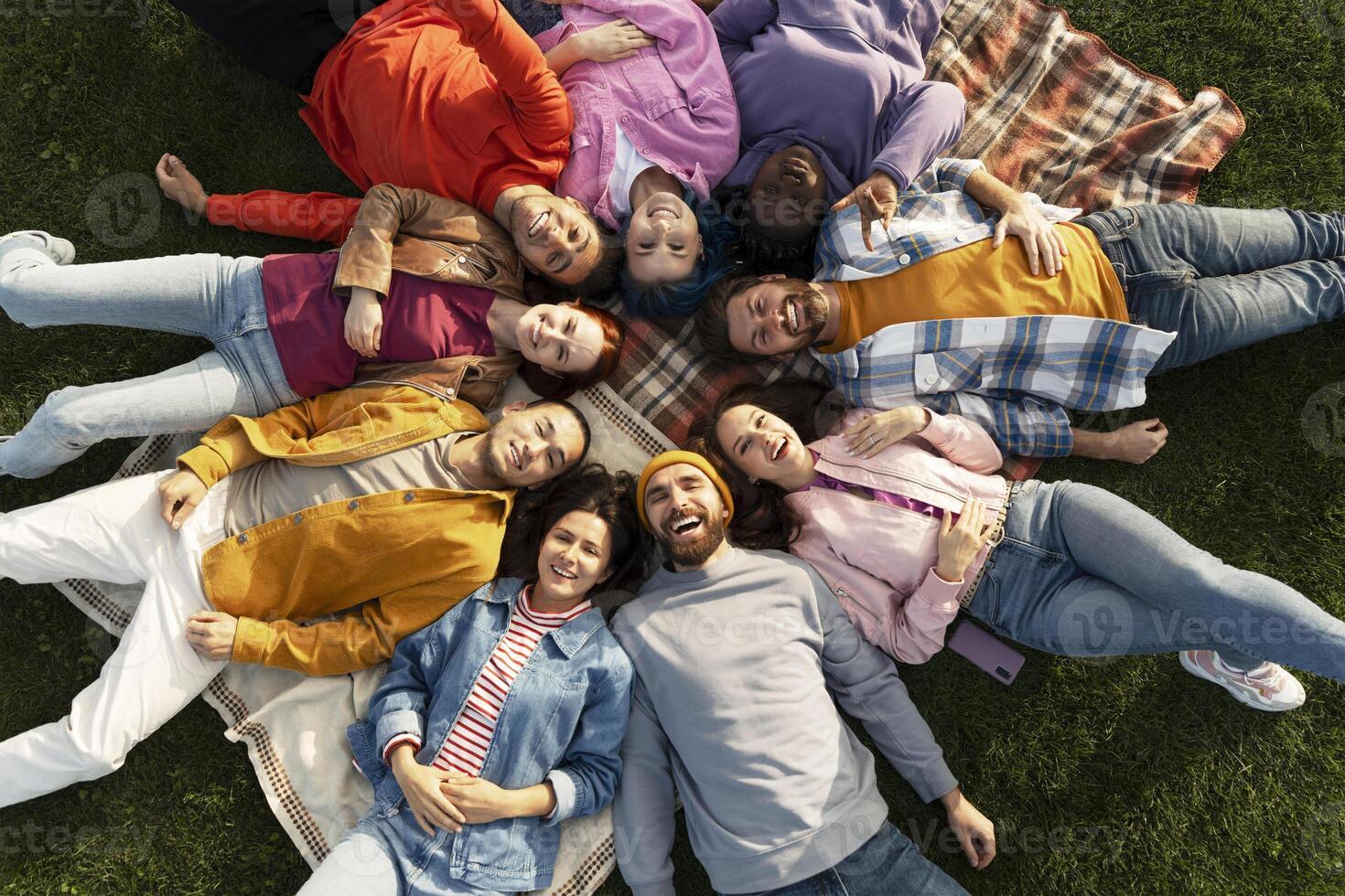 Diverse group of people lying in circle on grass smiling at camera photo