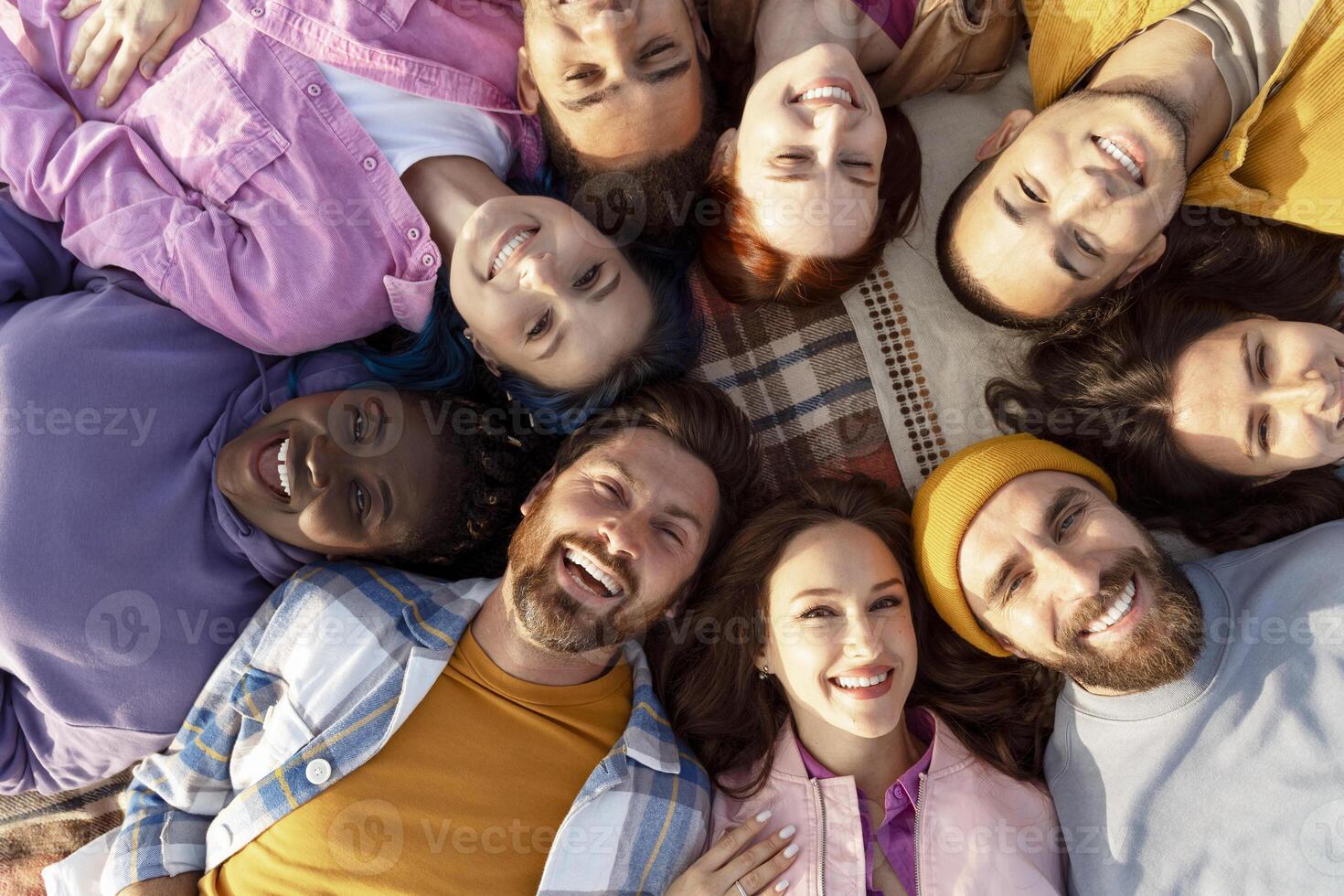Diverse group of people lying down in circle outdoors smiling at camera photo