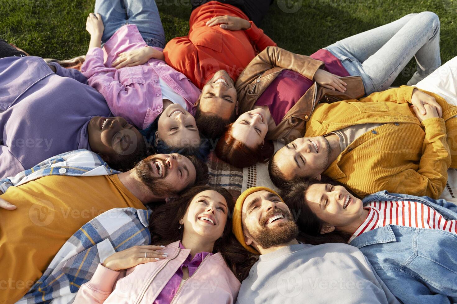 Diverse group of friends lying in circle on grass enjoying sunny day photo