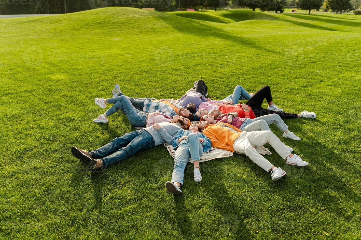 Group of friends relaxing lying down in circle on grass in park photo
